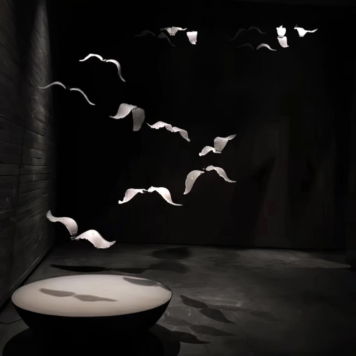 This Clérachic seagull chandelier scatters pale glass birds across a black room, their shadows falling on a low round table.