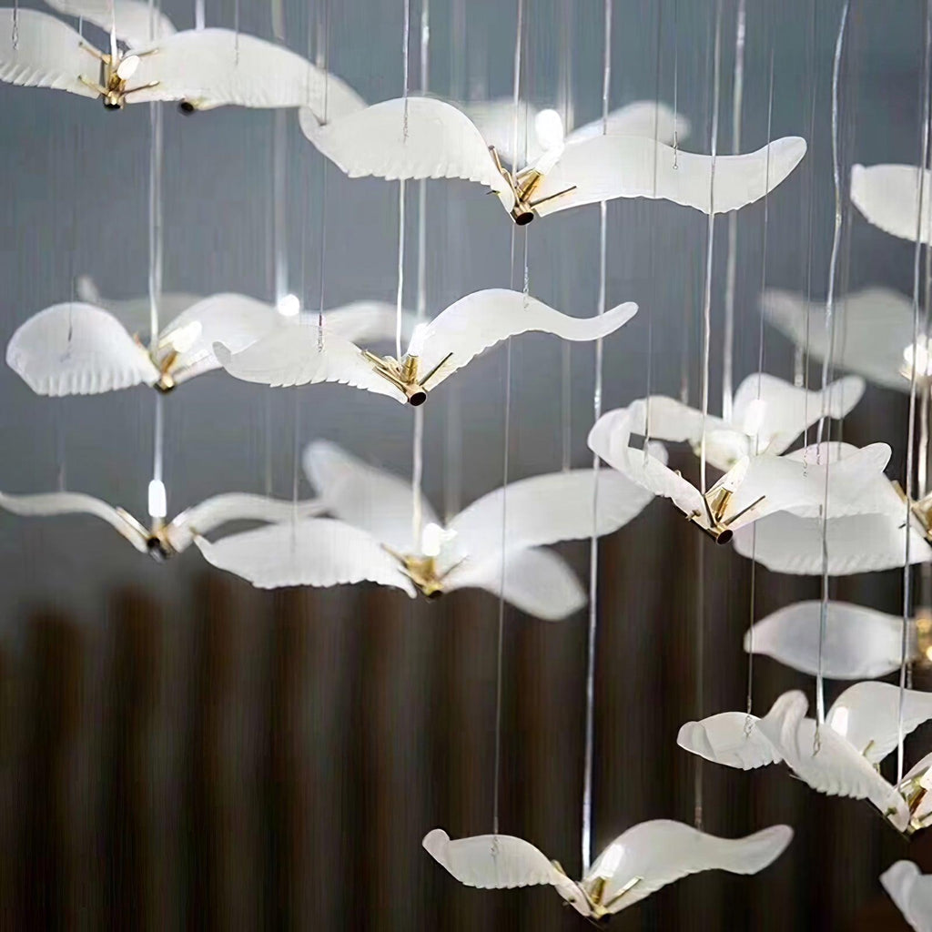 Close view of frosted glass gulls with gold bodies on this Clérachic chandelier, several glowing from within against a dark wall.