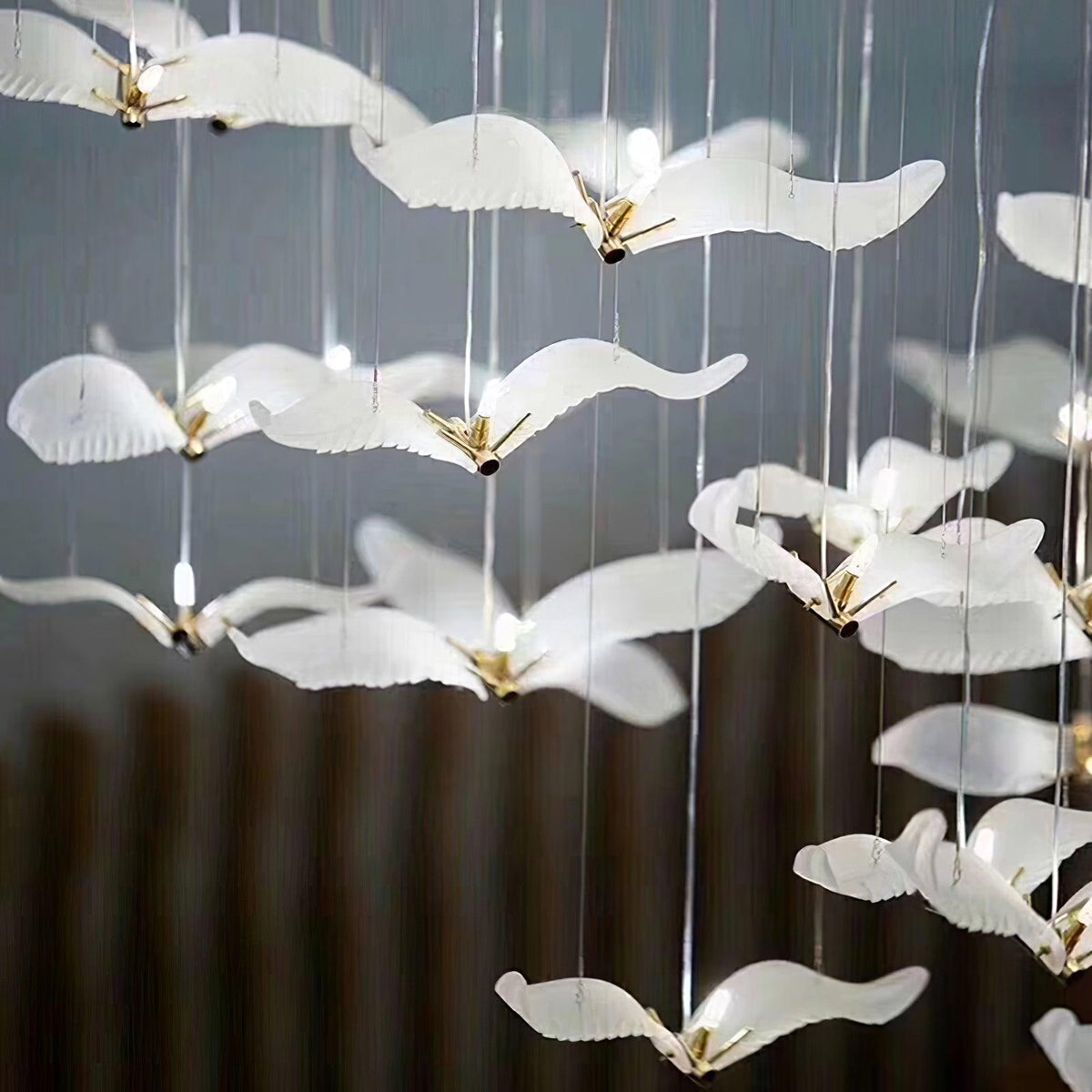 Close view of frosted glass gulls with gold bodies on this Clérachic chandelier, several glowing from within against a dark wall.