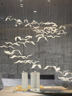 A swarm of Clérachic glass gulls hangs in a loose diagonal above a model of two towers on a pale marble desk.