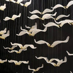 Close view of white glass seagulls with brass bodies on this Clérachic chandelier, hanging on fine cables against a black wall.