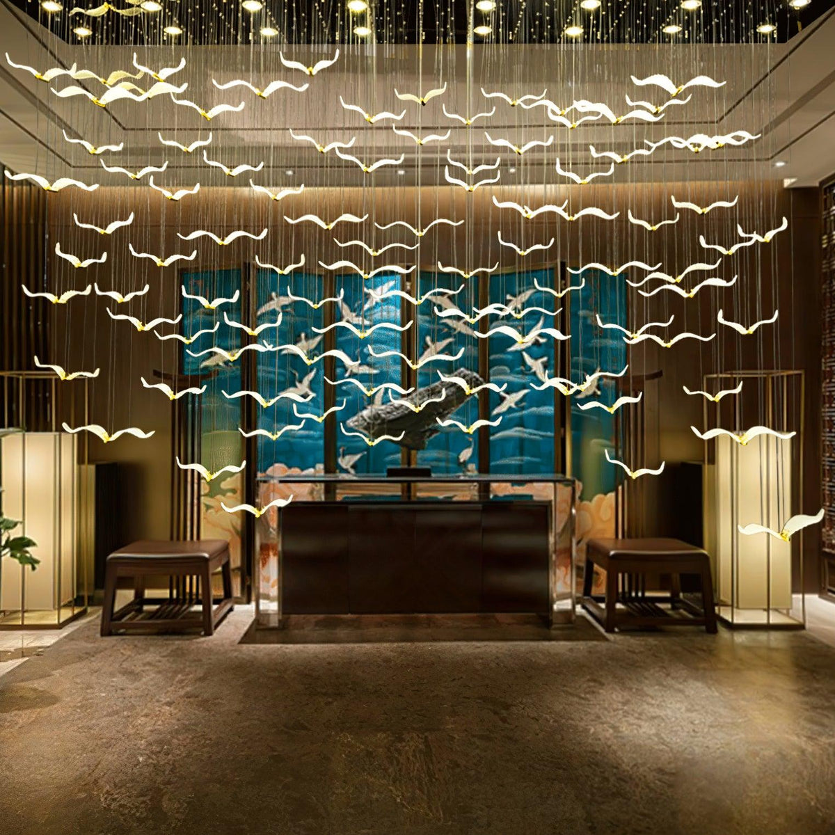 Warm light glows through the glass gulls of this Clérachic chandelier above a dark reception desk and a teal glass panel.