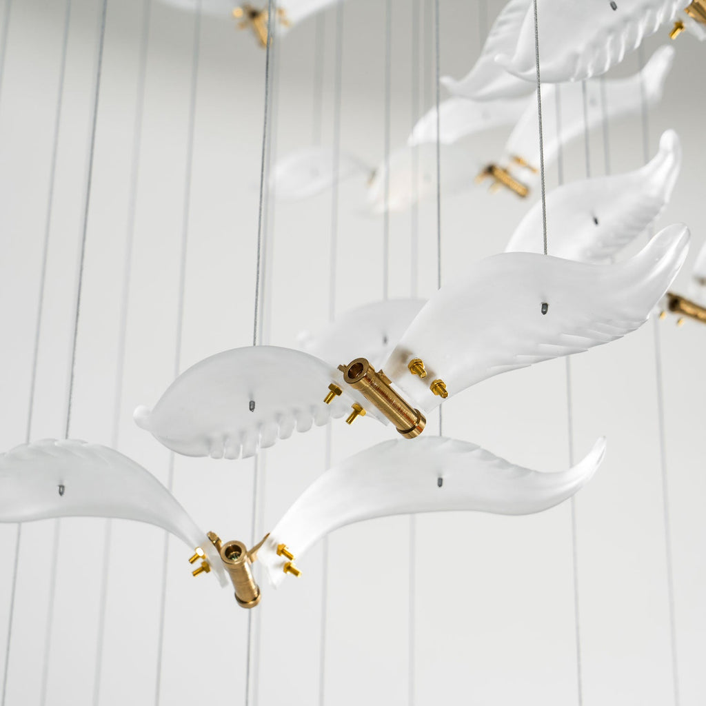 Close view of several frosted glass gulls with brass bodies on this Clérachic chandelier, hanging below fine cables.