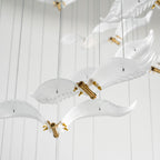 Close view of several frosted glass gulls with brass bodies on this Clérachic chandelier, hanging below fine cables.