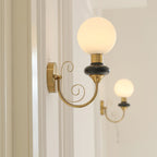A Clérachic wall light with a black collar and lit globe on a white panelled wall, with a second lit sconce behind it.