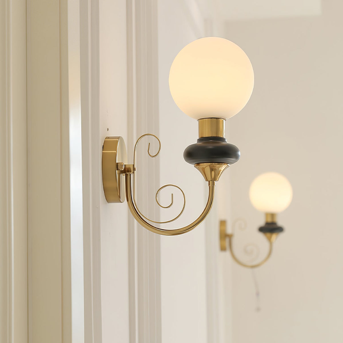 A Clérachic wall light with a black collar and lit globe on a white panelled wall, with a second lit sconce behind it.