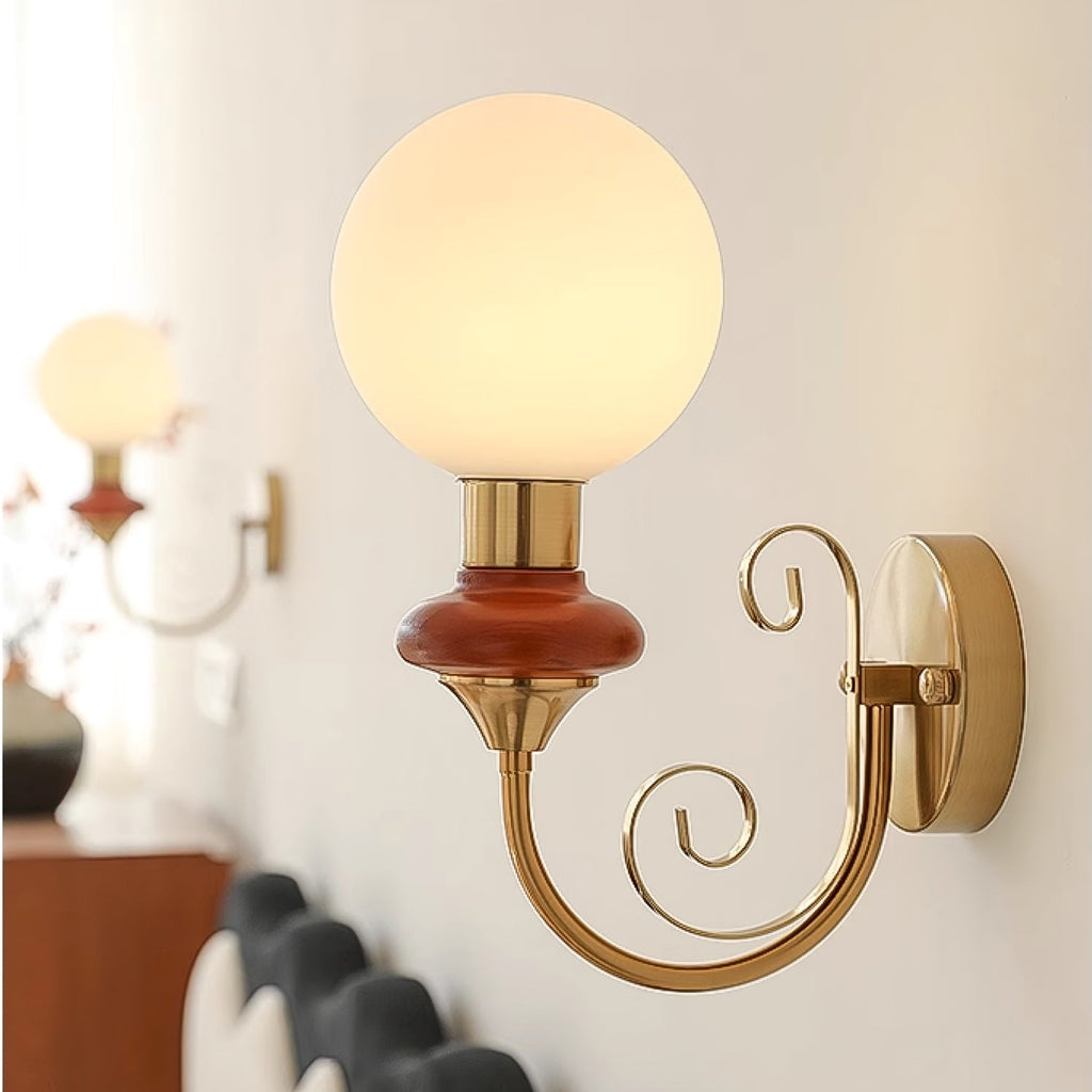Close, angled view of a Clérachic wall light with a mahogany collar, a large lit globe and a gold arm curling into spirals.
