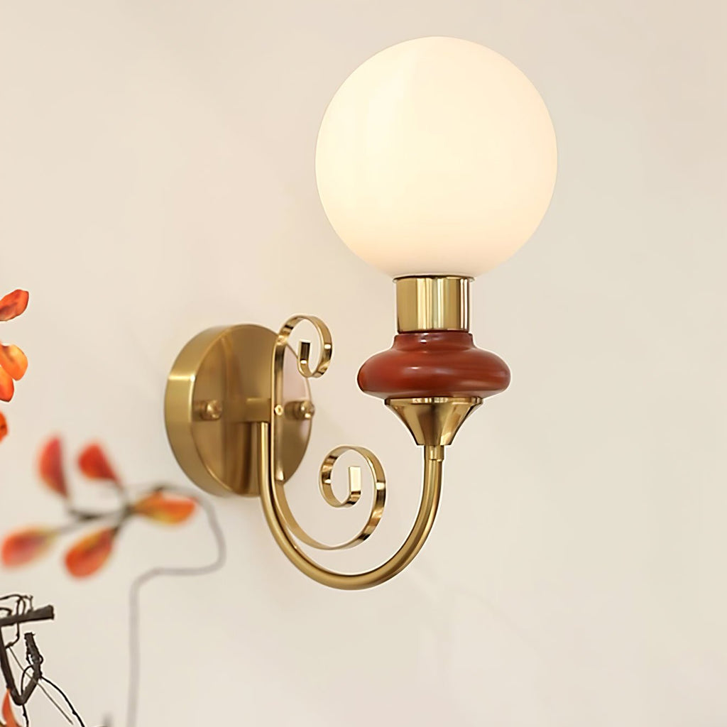 Mahogany-collared Clérachic wall light shown large in frame, its round gold backplate and scrolled arm against a cream wall.