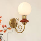 Mahogany-collared Clérachic wall light shown large in frame, its round gold backplate and scrolled arm against a cream wall.