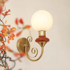 Mahogany-collared Clérachic wall light with a lit globe, framed by blurred orange autumn leaves on a cream wall.
