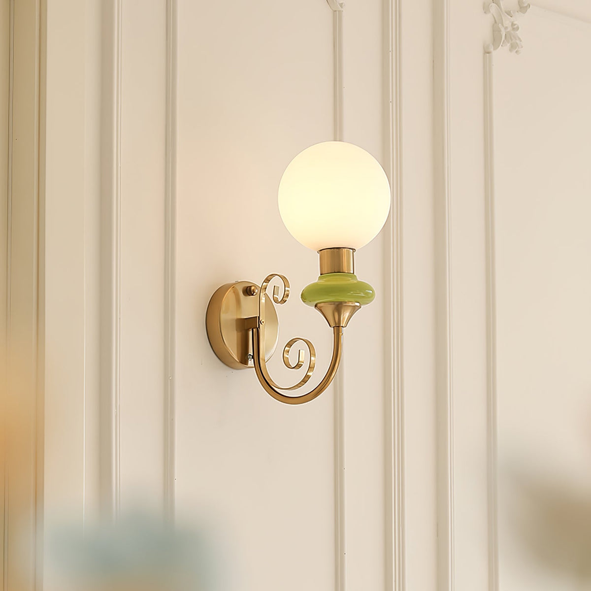 A Clérachic wall light with a green collar, its globe glowing softly against white wall panelling.