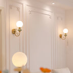 Two Clérachic wall lights with pale green collars flank a panelled white wall, with a large globe lamp glowing in the foreground.