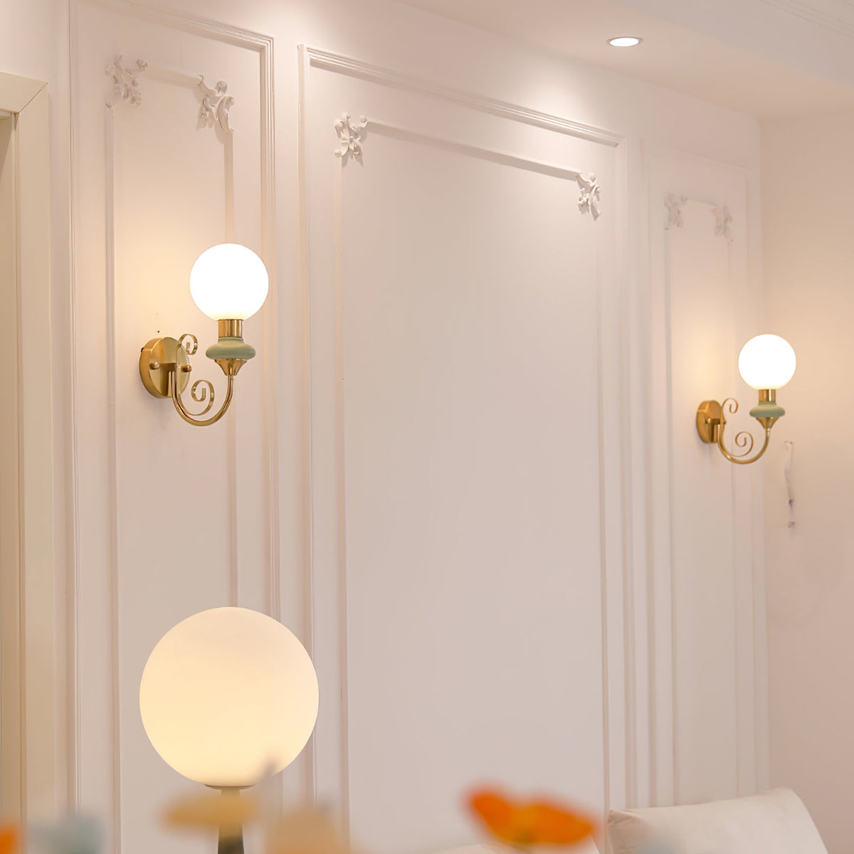 Two Clérachic wall lights with pale green collars flank a panelled white wall, with a large globe lamp glowing in the foreground.