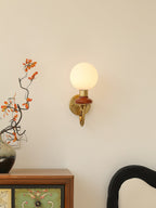 Clérachic wall light with a mahogany collar mounted above a painted wooden cabinet, with a branch of orange leaves beside it.
