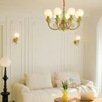 Living room with two Clérachic wall lights on panelled walls, a green and gold chandelier overhead, a black floor lamp and a cream sofa.