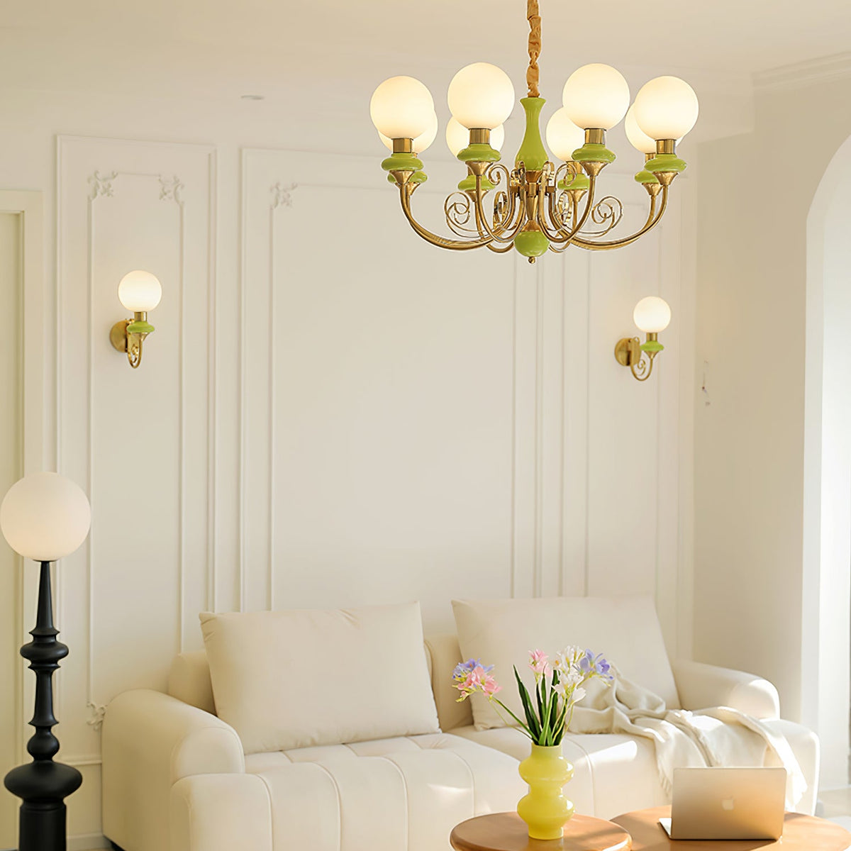 Living room with two Clérachic wall lights on panelled walls, a green and gold chandelier overhead, a black floor lamp and a cream sofa.