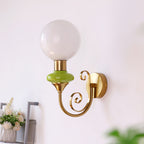 Green-collared Clérachic wall light with a clear-white globe, shown close up against a pale wall with flowers in the corner.