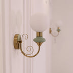 Close view of a Clérachic wall light with a pale green collar, its large globe and curled gold arm against a soft white wall.
