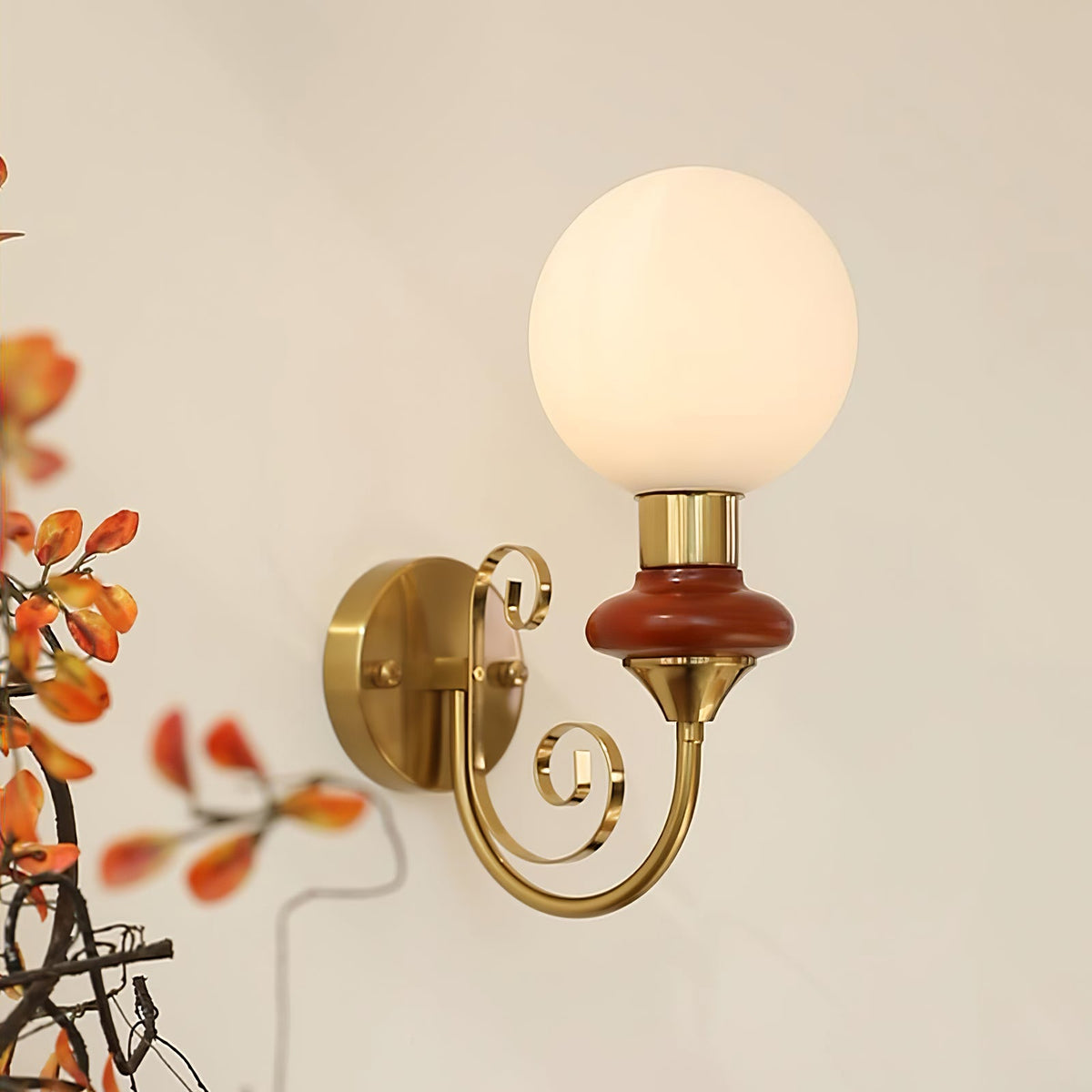 Mahogany-collared Clérachic wall sconce with a lit globe and orange autumn leaves in the foreground on a cream wall.