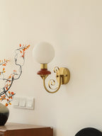 Clérachic wall light with a mahogany collar and unlit white globe on a cream wall, above a row of switches and a dark vase.