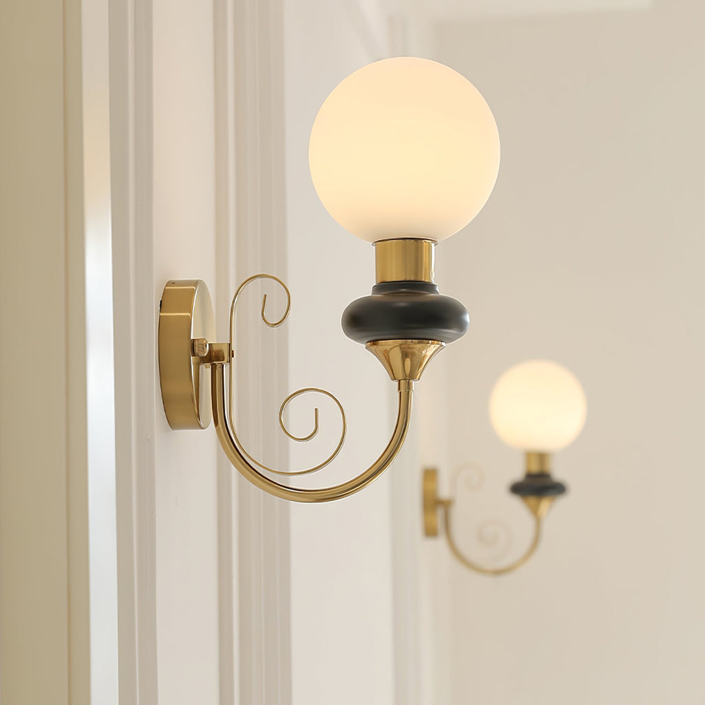 A Clérachic wall light with a black collar and lit globe beside a door frame, another sconce glowing in the background.