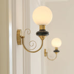 A Clérachic wall light with a black collar and lit globe beside a door frame, another sconce glowing in the background.