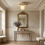 An ivory Clérachic glass sphere ceiling light above a hall console, with a gilt-framed mirror and a vase of dried lavender.