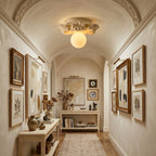 This Clérachic ceiling light glowing in a vaulted, cream-walled corridor lined with framed botanical prints and a long console.
