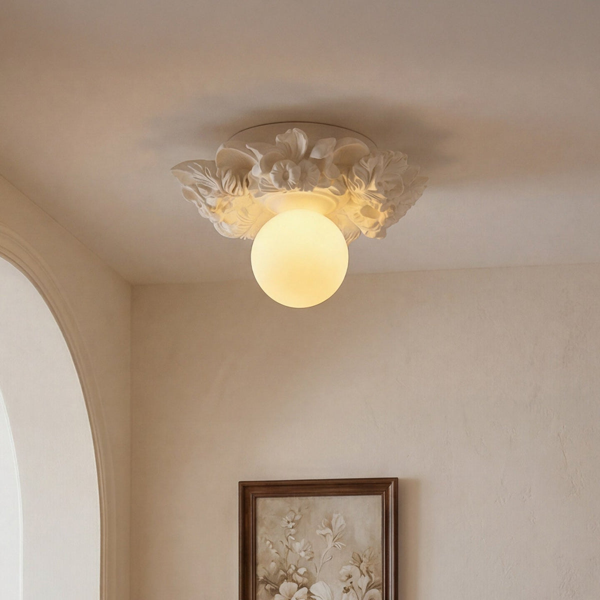 Looking up at the lit Clérachic glass sphere and its petalled resin collar, with an arched doorway and a framed print below.