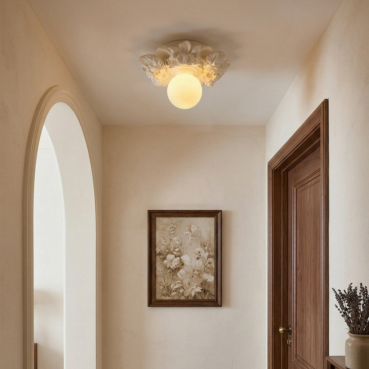 A Clérachic ceiling light lit in a hallway with an arched opening and a dark wood door, a framed floral print on the wall.