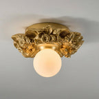 Gilded gold version of this Clérachic ceiling light on a grey ceiling, with a warm-lit frosted glass sphere below the flower collar.