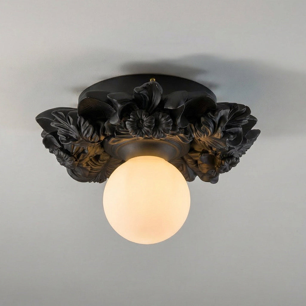 Matte black version of this Clérachic ceiling light on a grey ceiling, its dark resin flowers framing a warm-lit glass sphere.