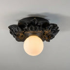 Matte black version of this Clérachic ceiling light on a grey ceiling, its dark resin flowers framing a warm-lit glass sphere.