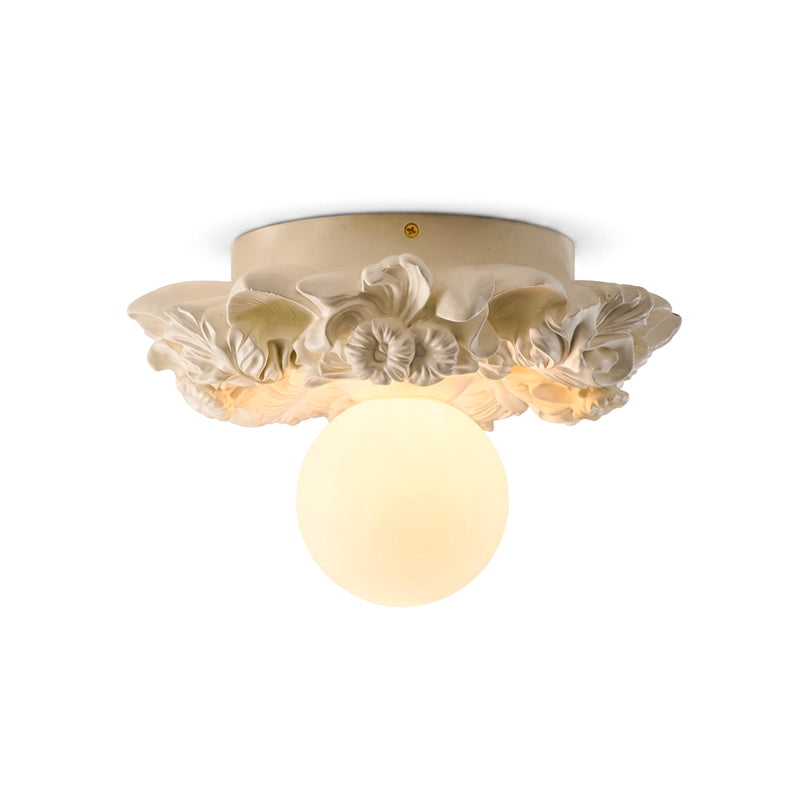 Ivory white Clérachic flush-mount light with a glowing glass sphere under its resin flower collar, on a white background.