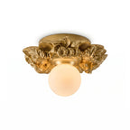 Gilded gold Clérachic flush-mount light with a glowing glass sphere under its resin flower collar, on a white background.