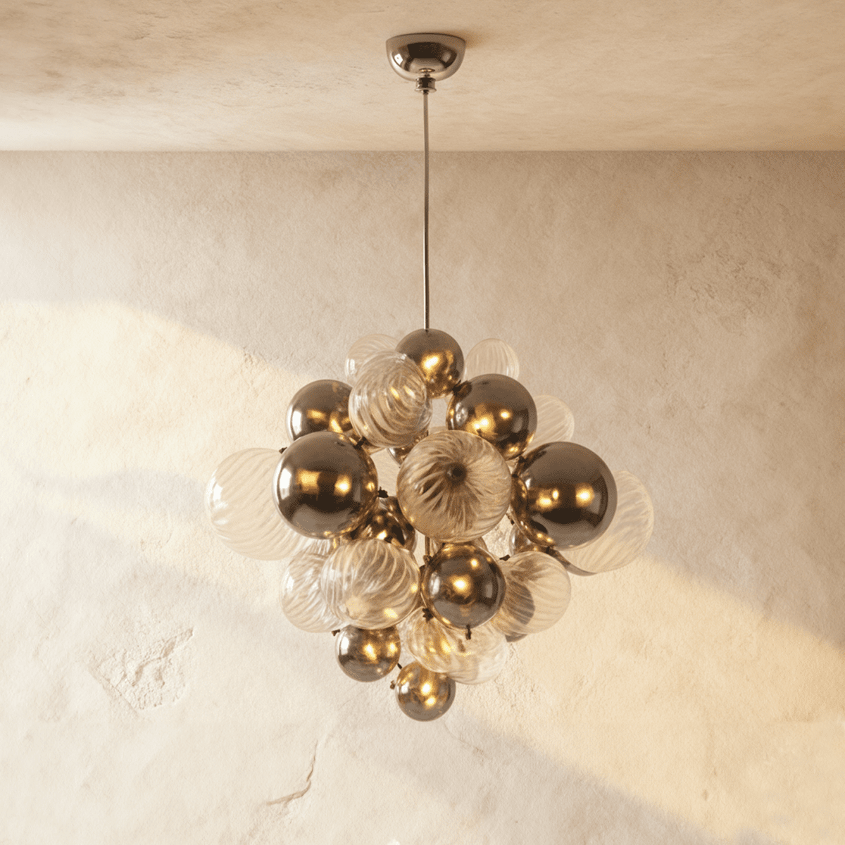 Clérachic chandelier of clear fluted glass spheres and mirror-finish metal spheres on a slim rod, glowing on a limewash wall.