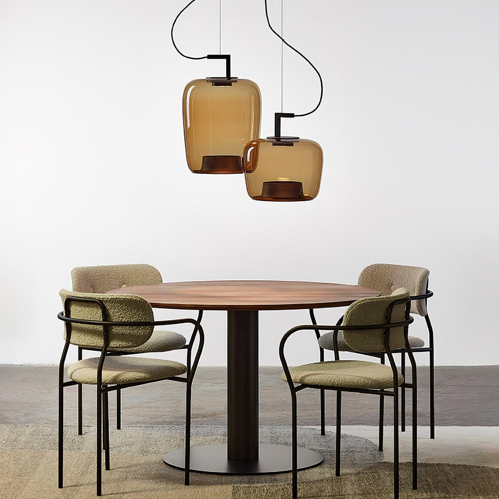 Two amber glass Clérachic pendants hang at different heights over a round walnut table with olive boucle chairs.