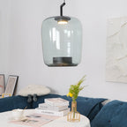 Tall grey-green glass Clérachic pendant with a black cap above a round table with books, a gold wire vase and a blue sofa.