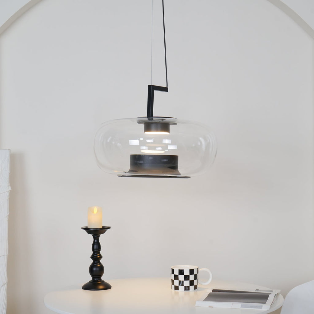 Clear glass Clérachic pendant with a black stem bracket over a candlestick, a checked mug and a magazine on a white table.