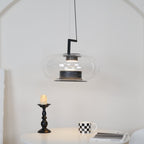 Clear glass Clérachic pendant with a black stem bracket over a candlestick, a checked mug and a magazine on a white table.