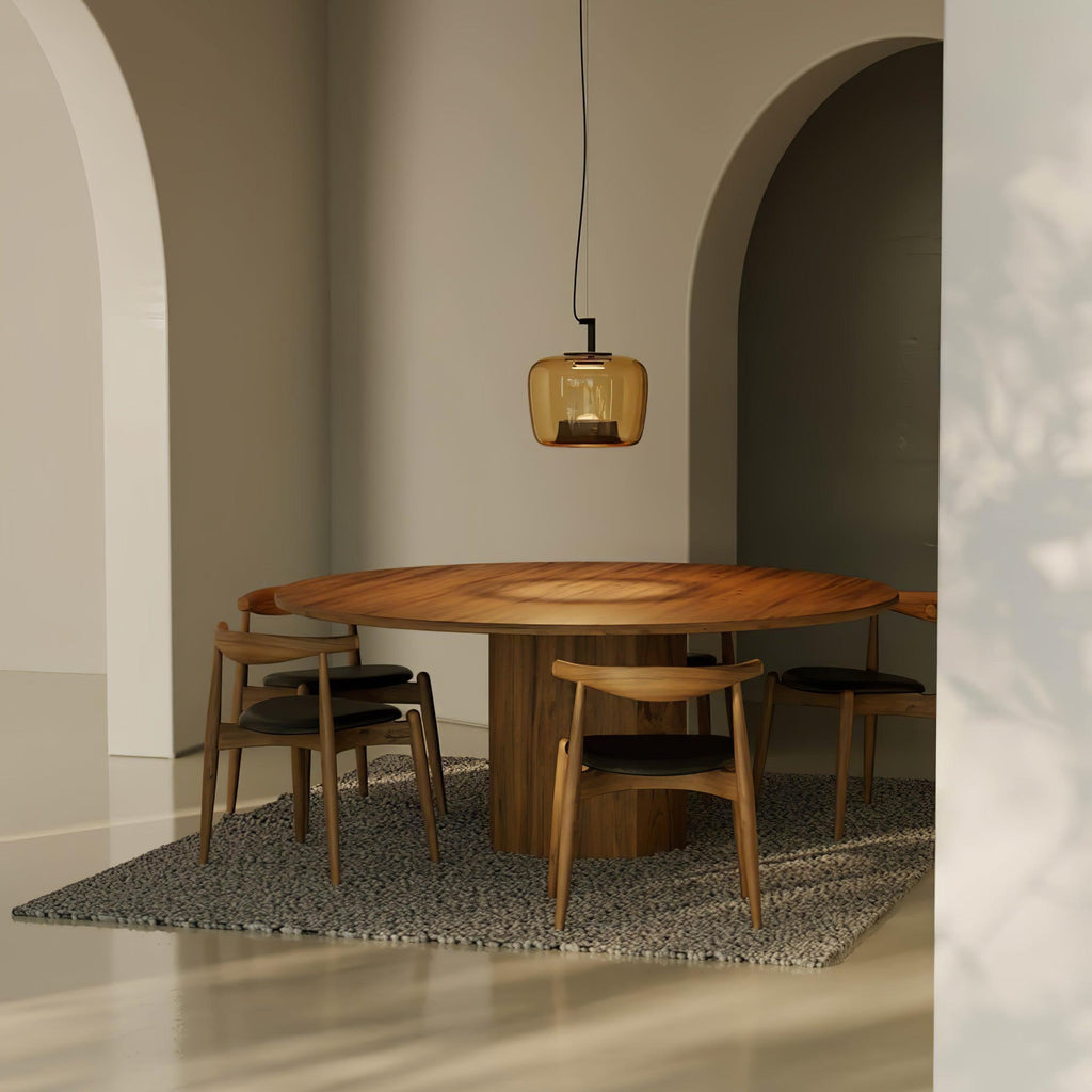Small amber Clérachic pendant over a round walnut table with wooden chairs, in a room with plaster arches and a patterned rug.