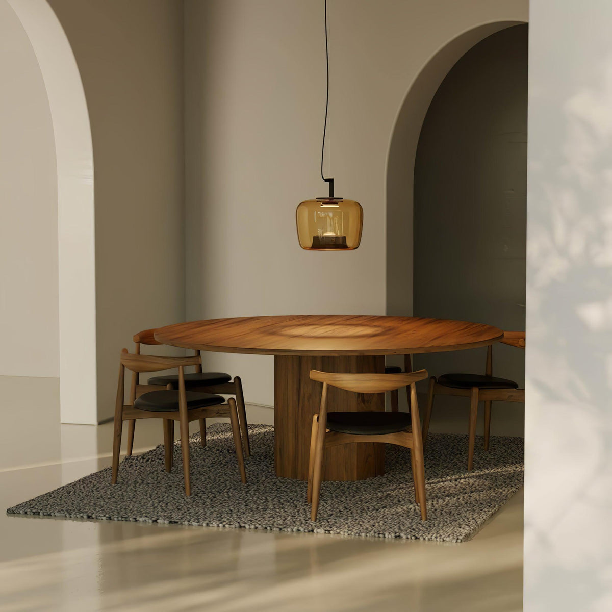 Small amber Clérachic pendant over a round walnut table with wooden chairs, in a room with plaster arches and a patterned rug.