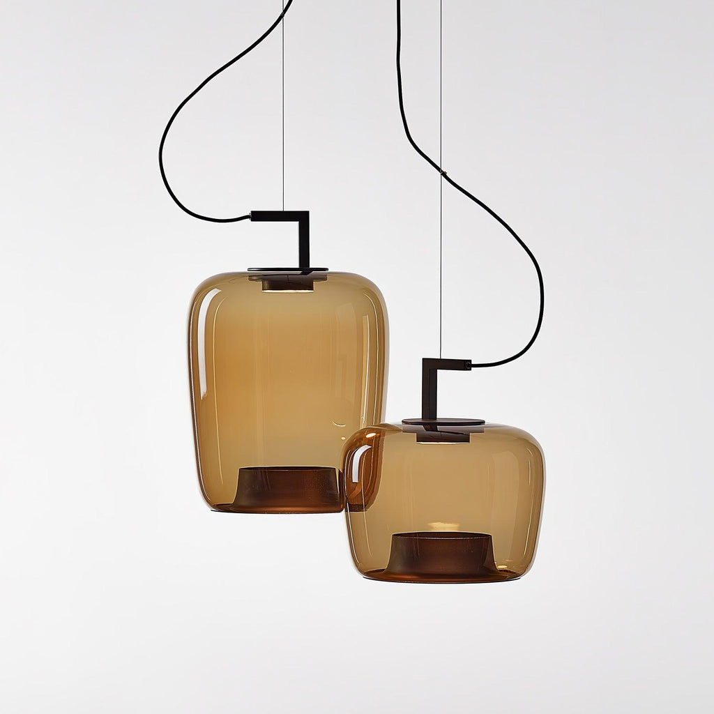 Two amber glass Clérachic pendants, one tall and one rounded, on separate black brackets against a pale backdrop.