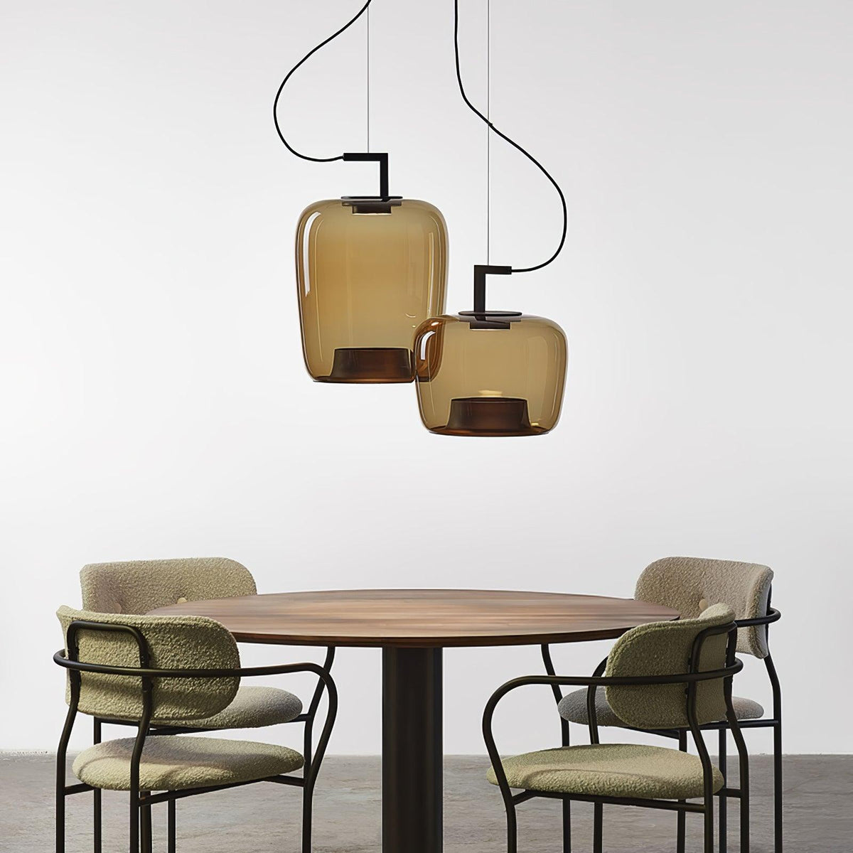 Two amber glass Clérachic pendants hang above a round walnut dining table with four green boucle chairs.