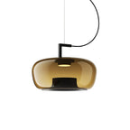 Wide amber glass Clérachic pendant with a black bracket and a warm light at its centre, on a white backdrop.