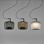 Three Clérachic pendants in smoke grey, amber and foggy white glass hang side by side against a mid-grey backdrop.