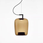 Tall amber glass Clérachic pendant with a black bracket and a glowing top, shown on a white backdrop.