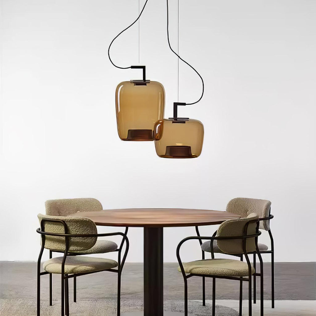 Two small amber glass Clérachic pendants hang above a round table and four boucle chairs on a grey floor.