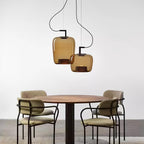 Two small amber glass Clérachic pendants hang above a round table and four boucle chairs on a grey floor.