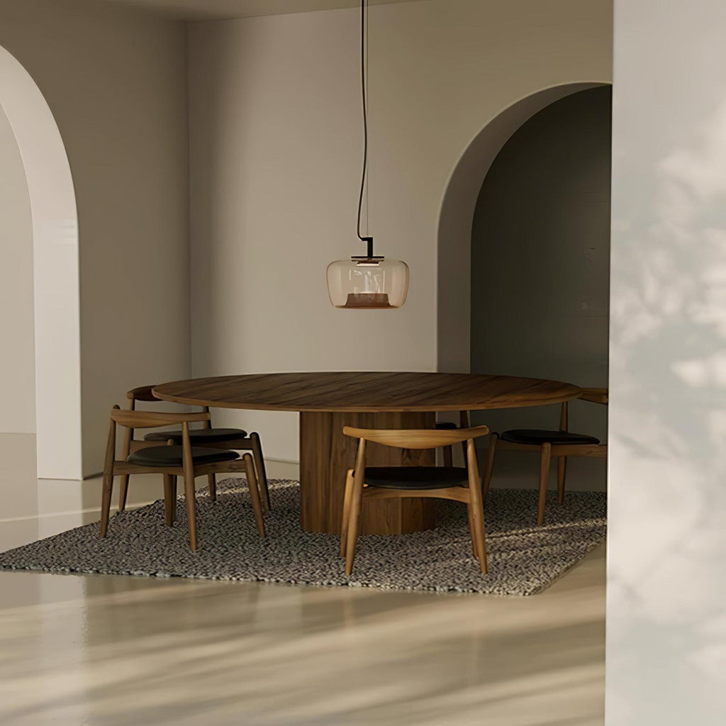 Small amber Clérachic pendant over a large round wooden table in an arched room with a speckled rug.